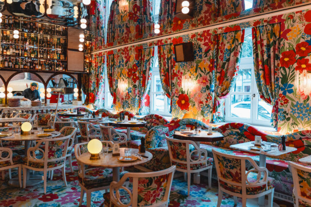 Ein bunter Innenraum eines Restaurants in München mit Blumentapete und kitschigen Details.