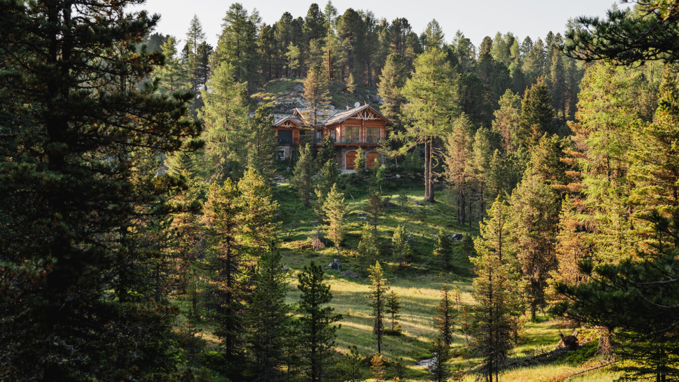 Ein Holzhaus in der Ferne, umgeben von grünem Wald und einem kleinen Bach auf der Turracher Höhe.
