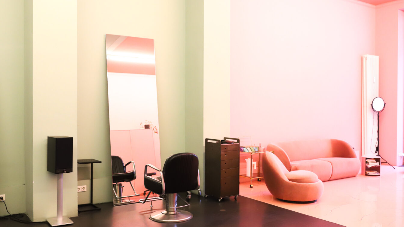 Foto eines Friseur in Berlin mit minimalistischer Einrichtung. Man sieht einen Friseurstuhl vor einem an der Wand gelehnten Spiegel und eine Couch daneben.