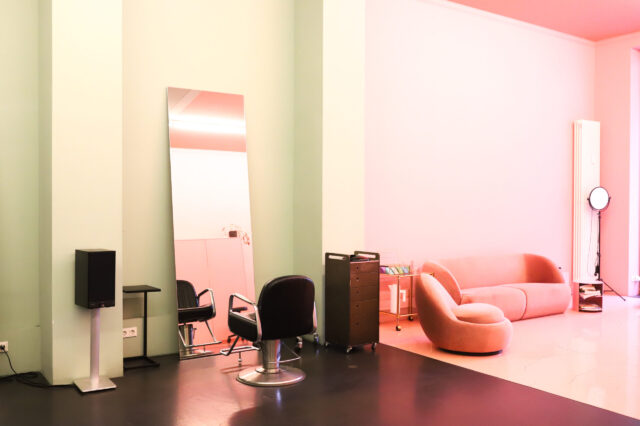 Foto eines Friseur in Berlin mit minimalistischer Einrichtung. Man sieht einen Friseurstuhl vor einem an der Wand gelehnten Spiegel und eine Couch daneben.