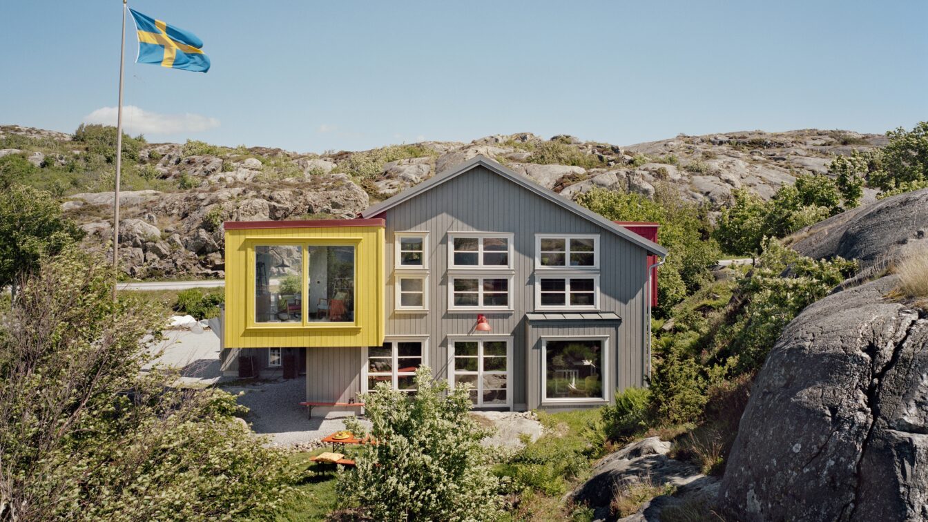Modernes Gästehaus Lådfabriken an der schwedischen Westküste – stilvolles Architektenhaus mit farbigen Akzenten inmitten felsiger Landschaft und Natur, mit schwedischer Flagge im Vordergrund.