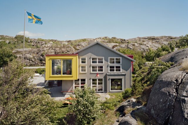 Modernes Gästehaus Lådfabriken an der schwedischen Westküste – stilvolles Architektenhaus mit farbigen Akzenten inmitten felsiger Landschaft und Natur, mit schwedischer Flagge im Vordergrund.