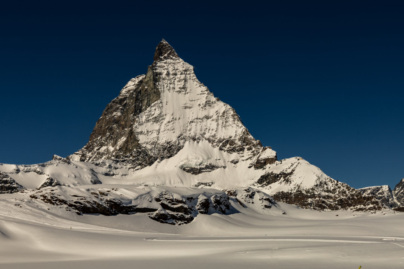 Schneebedecktes Matterhorn vor tiefblauem Himmel in der Schweiz, fotografiert bei klarem Winterwetter. Im Vordergrund eine weite, unberührte Schneelandschaft.