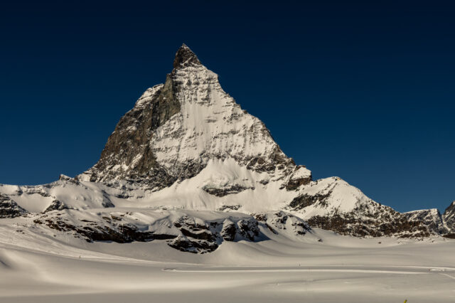 Schneebedecktes Matterhorn vor tiefblauem Himmel in der Schweiz, fotografiert bei klarem Winterwetter. Im Vordergrund eine weite, unberührte Schneelandschaft.