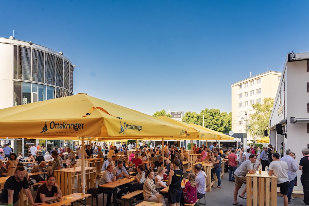 Menschen sitzen im Sommer unter Schirmen am Gelände der Ottakringer Brauerei