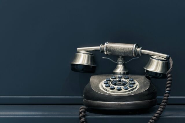 Ein altes, schwarzes Kabeltelefon vor einem dunkelblauen Hintergrund.