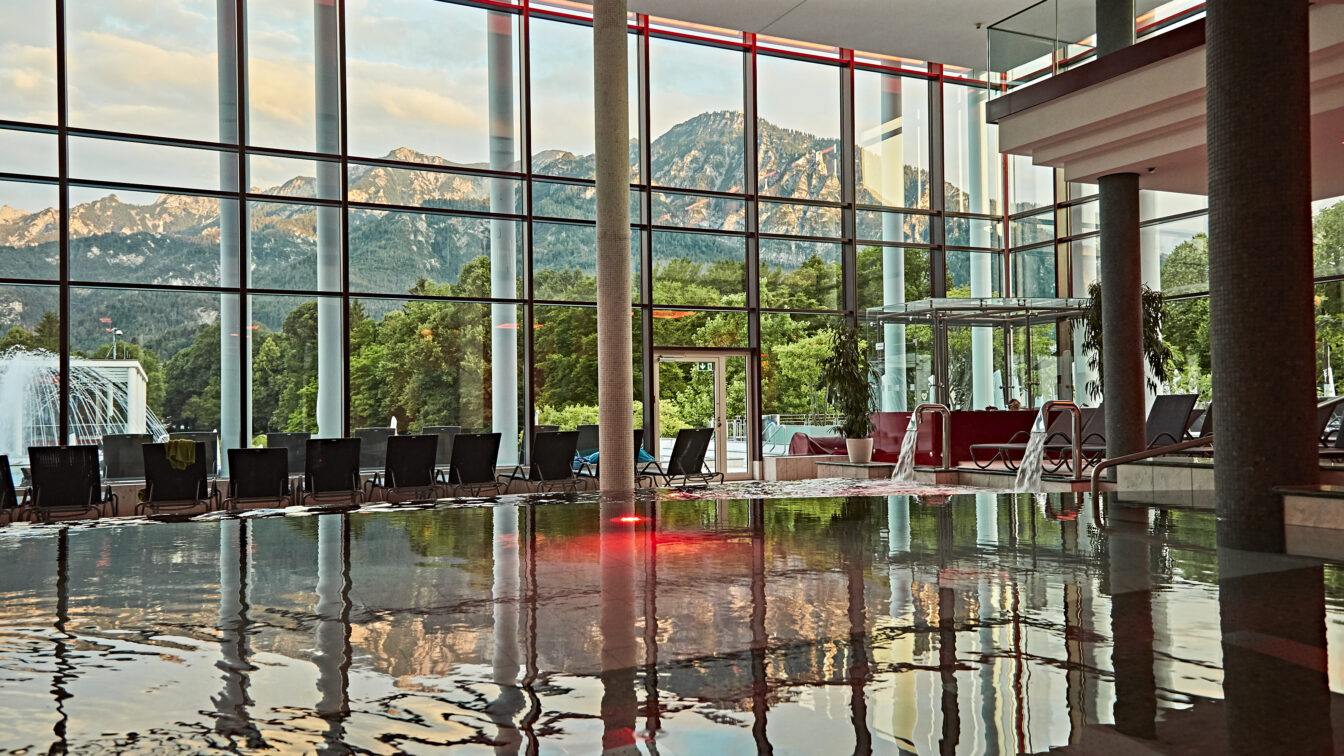 Eine Glasfassade, die sich im Wasser eines Pools spiegelt.