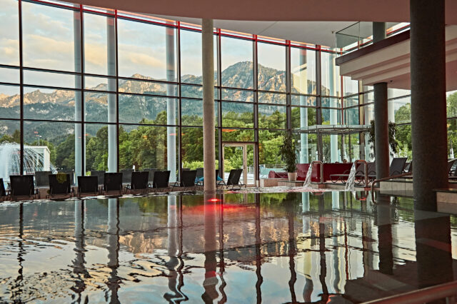 Eine Glasfassade, die sich im Wasser eines Pools spiegelt.