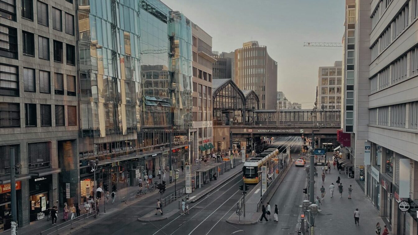 Foto einer Straßenschlucht, im Hintergrund sieht man Bahnschienen mit der Aufschrift Bahnhof Friedrichstraße.