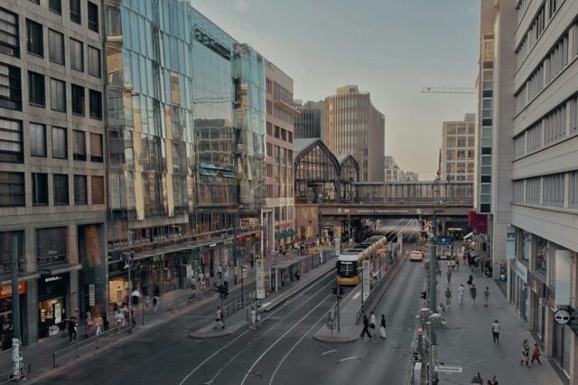 Foto einer Straßenschlucht, im Hintergrund sieht man Bahnschienen mit der Aufschrift Bahnhof Friedrichstraße.