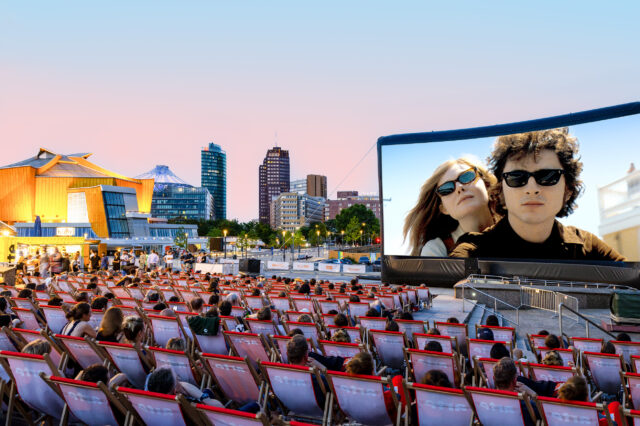 Freiluftkino in Berlin mit unzähligen Liegestühlen davor. Im Hintergrund sind Hochhäuser zu sehen.