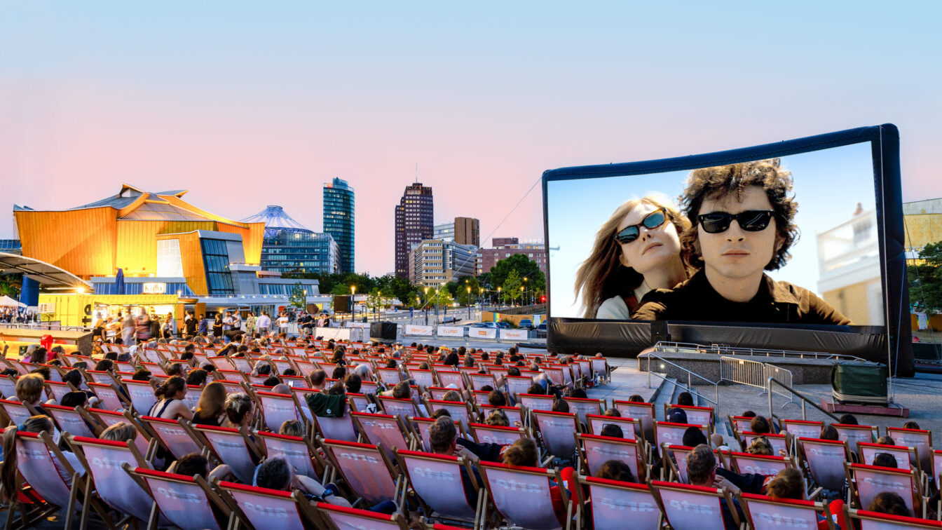 Freiluftkino in Berlin mit unzähligen Liegestühlen davor. Im Hintergrund sind Hochhäuser zu sehen.