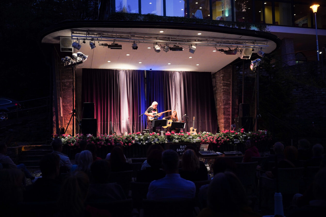 Sommerabend-Konzert beim ‚Summer Jazz in the City‘ in Bad Gastein – stimmungsvoller Auftritt eines Gitarrenduos auf blumengeschmückter Bühne im Freien, beleuchtet vor nächtlicher Kulisse mit Publikum im Vordergrund.
