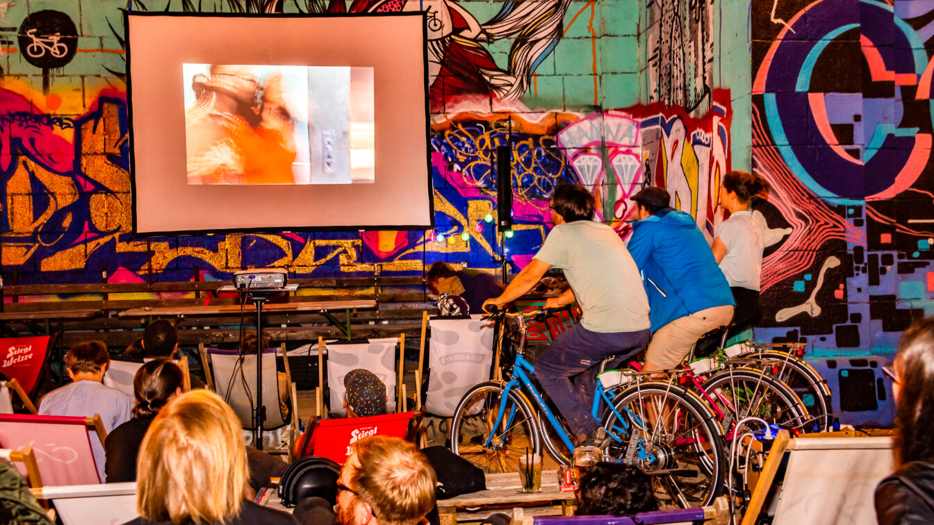 Menschen auf Liegestühlen und Fahrrädern, die einen Film schauen.