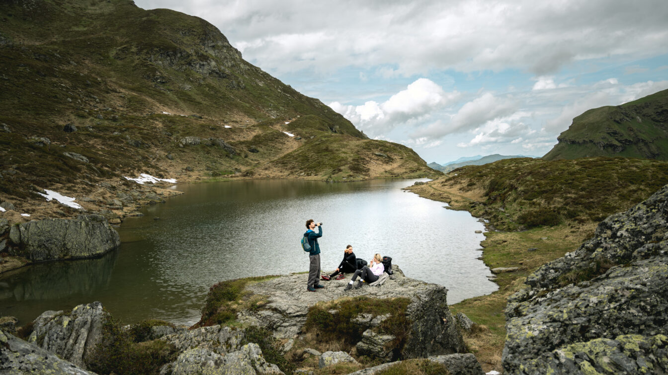 Drei Personen wandern in den Bergen und rasten am Bergsee