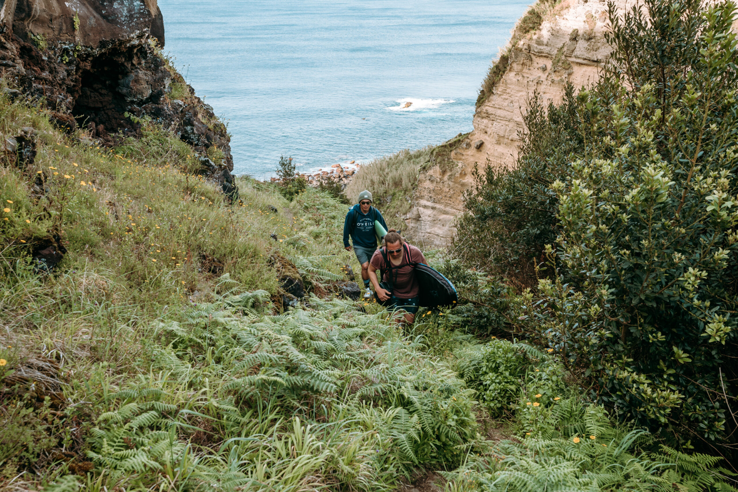 Personen wandern beim Surftrip auf den Azoren. Man sieht das Meer im Hintergrund.