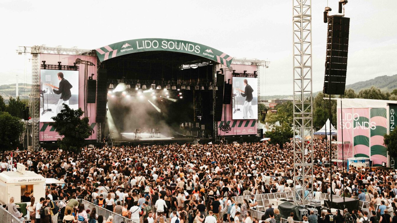 Großes Musikfestival LIDO SOUNDS 2025 in Linz mit Menschenmenge vor der Hauptbühne, Live-Konzert auf der Bühne mit LED-Leinwänden, Sommerstimmung, Festivalbesucher:innen und Bergen im Hintergrund – Open-Air-Event in Oberösterreich.