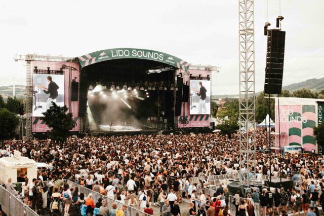 Großes Musikfestival LIDO SOUNDS 2025 in Linz mit Menschenmenge vor der Hauptbühne, Live-Konzert auf der Bühne mit LED-Leinwänden, Sommerstimmung, Festivalbesucher:innen und Bergen im Hintergrund – Open-Air-Event in Oberösterreich.