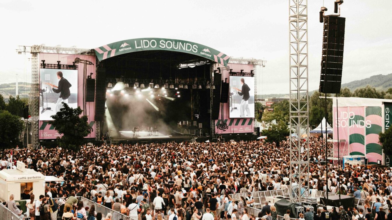Großes Musikfestival LIDO SOUNDS 2025 in Linz mit Menschenmenge vor der Hauptbühne, Live-Konzert auf der Bühne mit LED-Leinwänden, Sommerstimmung, Festivalbesucher:innen und Bergen im Hintergrund – Open-Air-Event in Oberösterreich.