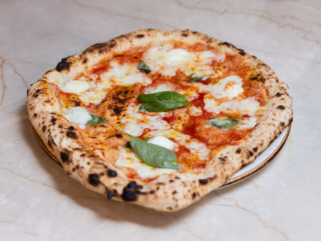 Nahaufnahme einer frisch gebackenen Pizza Margherita mit geschmolzenem Mozzarella, Tomatensauce und frischen Basilikumblättern auf einem hellen Marmortisch.