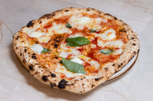 Nahaufnahme einer frisch gebackenen Pizza Margherita mit geschmolzenem Mozzarella, Tomatensauce und frischen Basilikumblättern auf einem hellen Marmortisch.