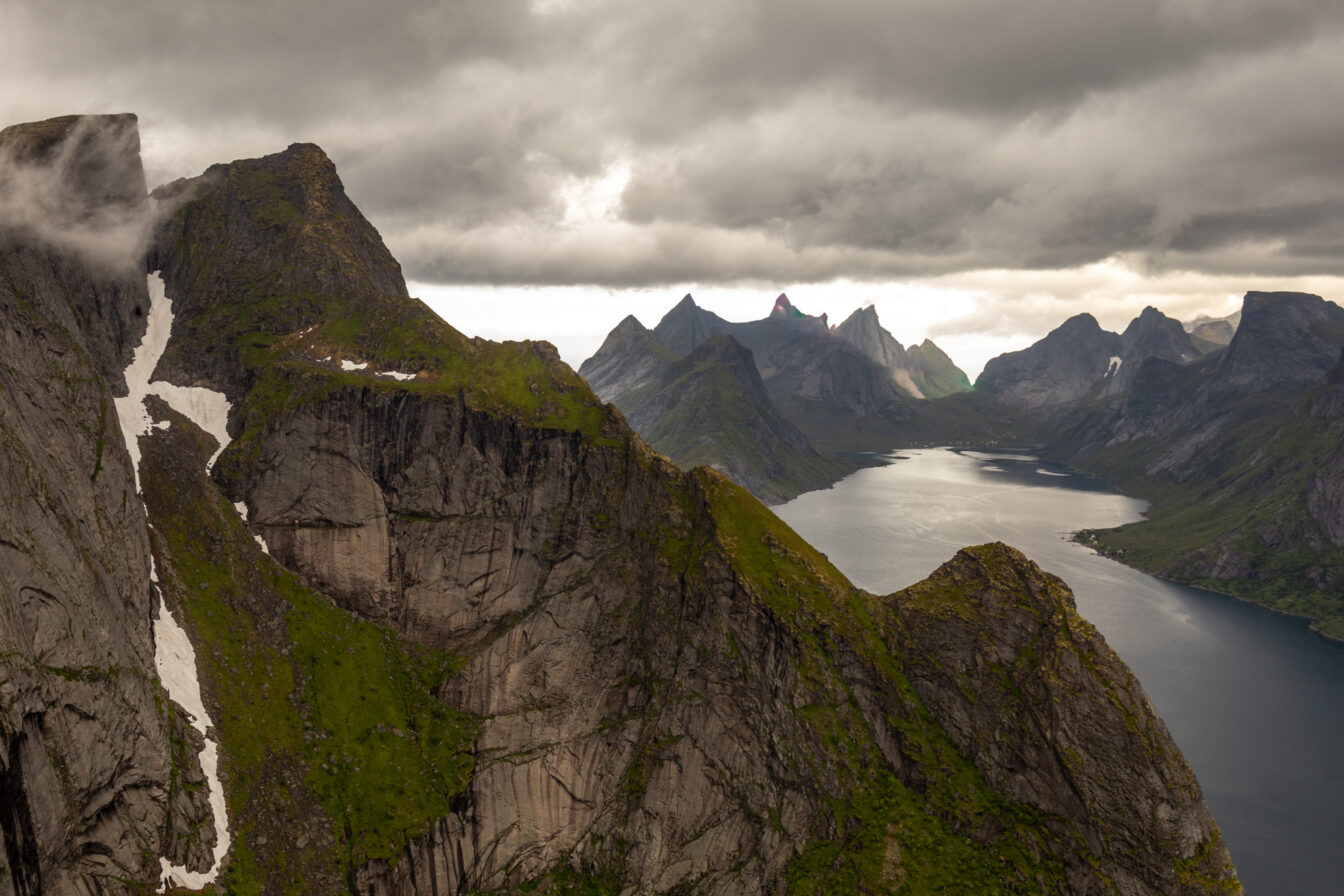 Dramatische Aussicht vom Reinebringen auf die zerklüftete Berglandschaft der Lofoten mit Fjordblick, markanten Felsformationen und tief hängenden Wolken – Naturwunder in Nordnorwegen.