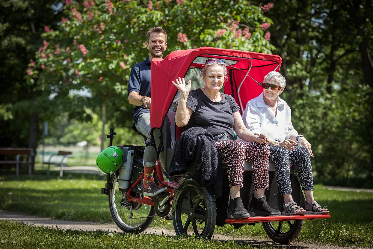 Zwei ältere Personen werden von einer anderen Person in einer Fahrrad-Rikscha gefahren