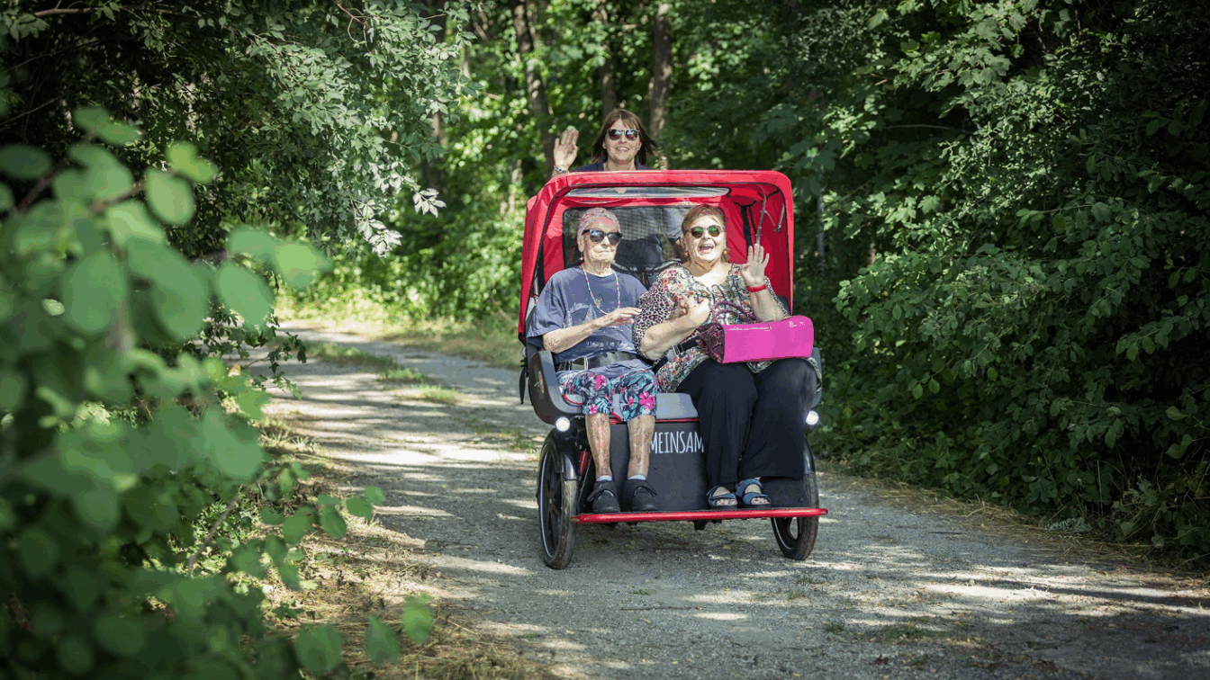 Zwei ältere Personen werden von einer anderen Person in einer Fahrrad-Rikscha gefahren