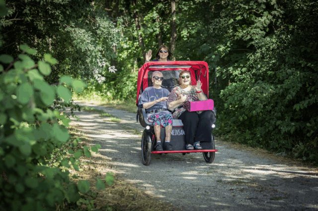 Zwei ältere Personen werden von einer anderen Person in einer Fahrrad-Rikscha gefahren