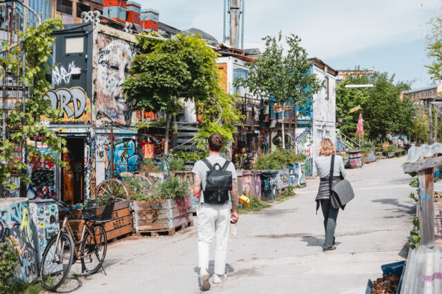Zwei Personen, die über ein begrüntes Areal aus alten Containern spazieren.