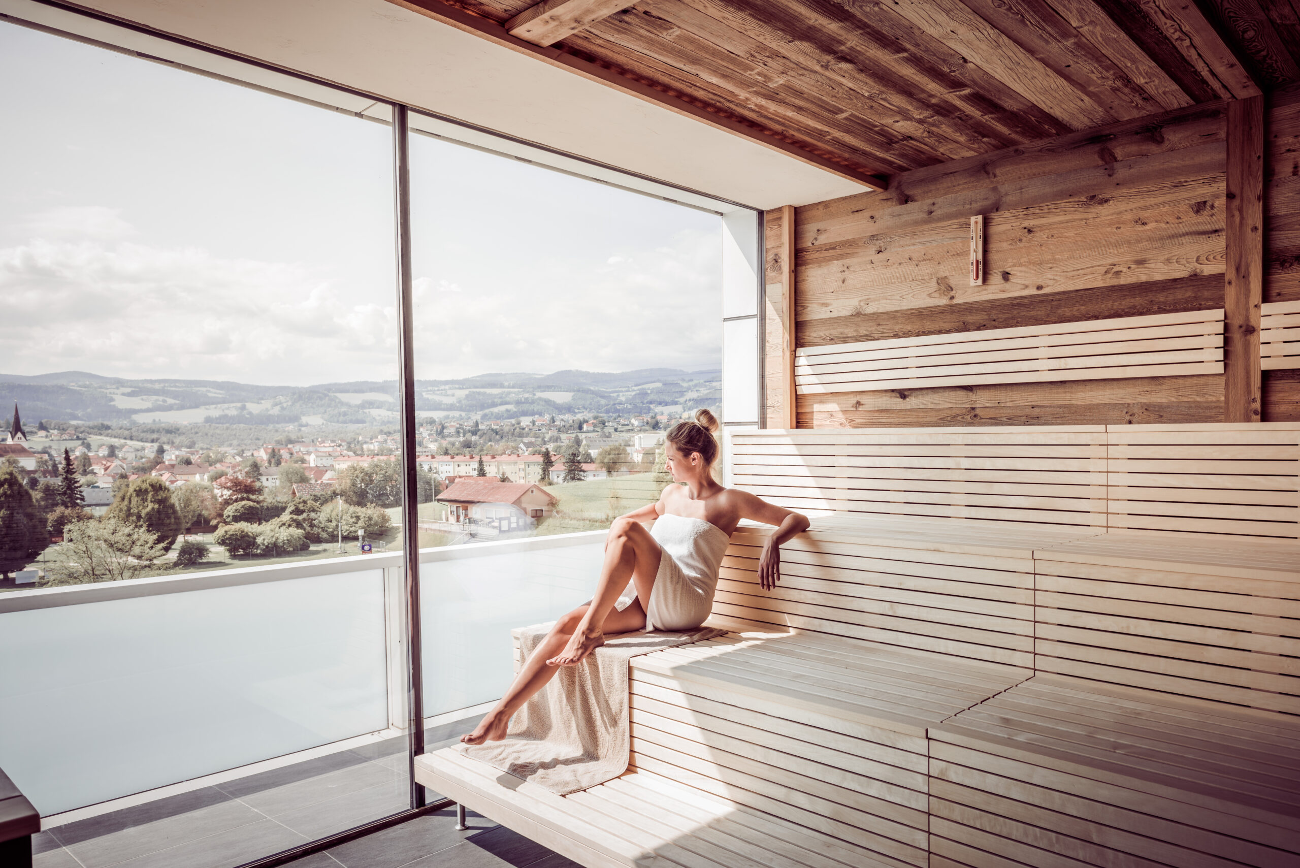 Eine Frau sitzt in der Sauna und schaut durch ein Panoramafenster.