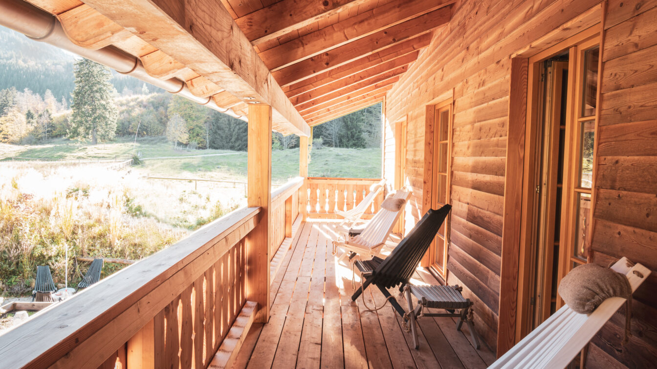 Gemütliche Holzveranda mit Liegestühlen in einer Berghütte in den Alpen bei Sonnenschein.