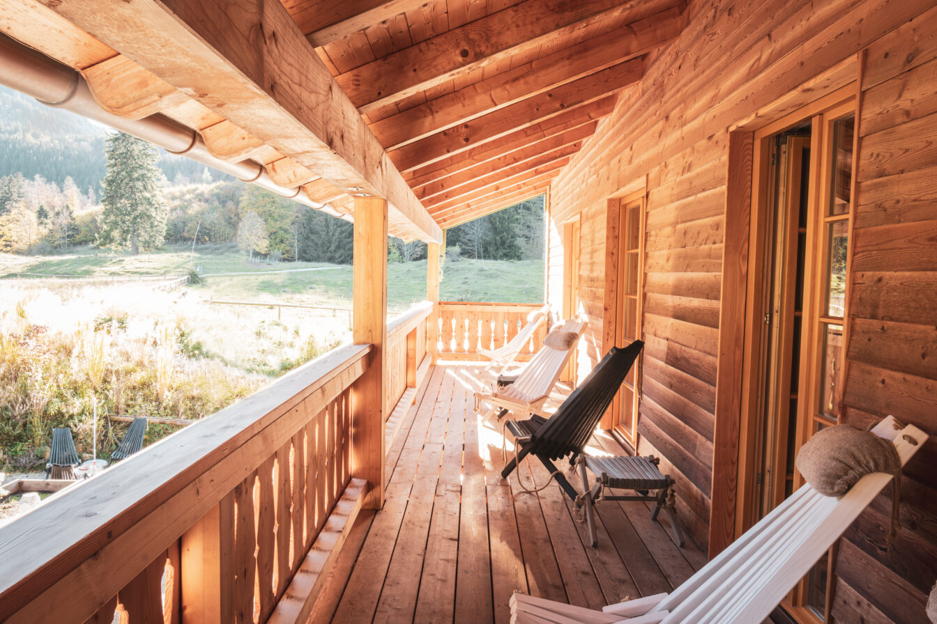 Gemütliche Holzveranda mit Liegestühlen in einer Berghütte in den Alpen bei Sonnenschein.