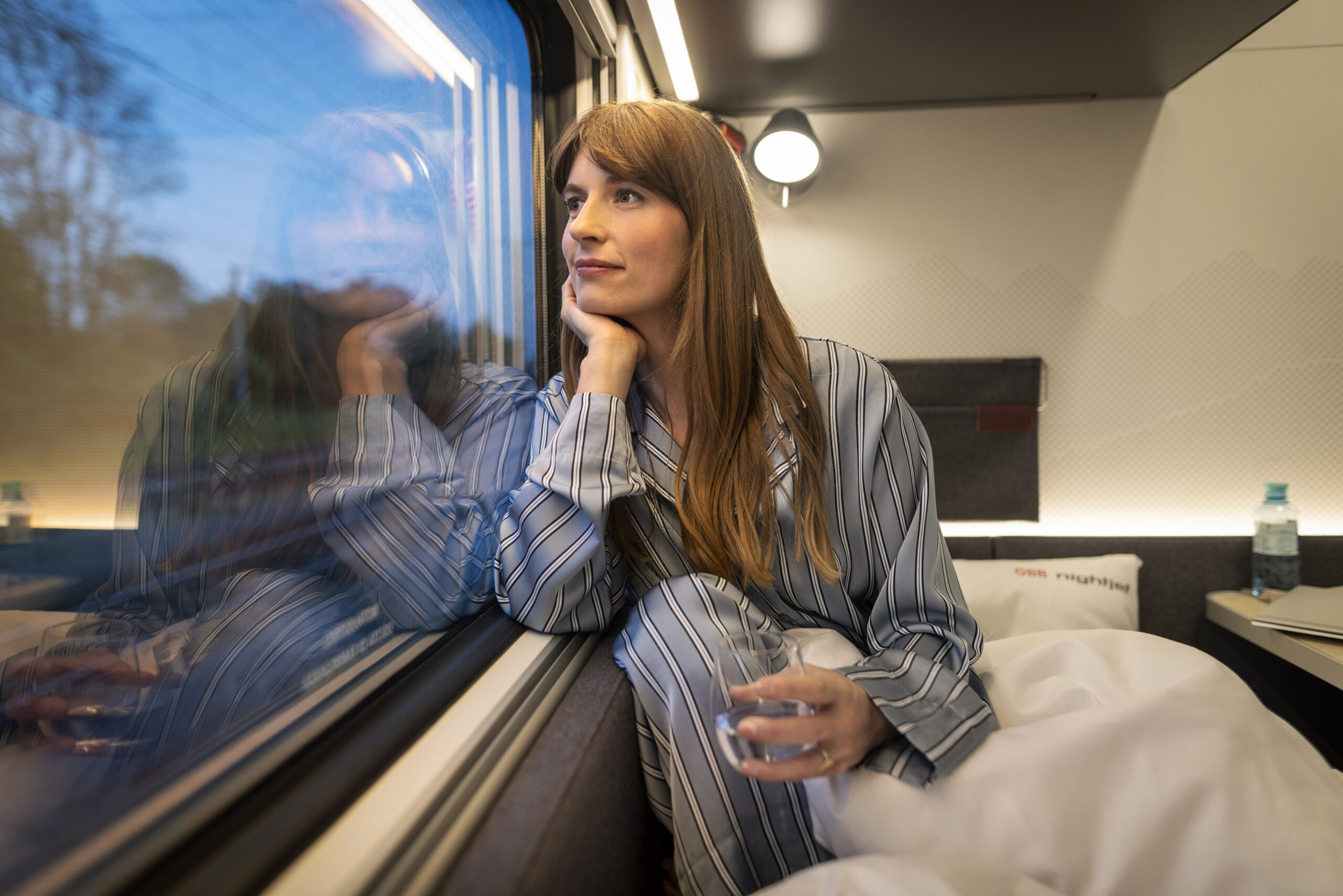 Frau schaut im Schlafabteil eines Zuges aus dem Fenster