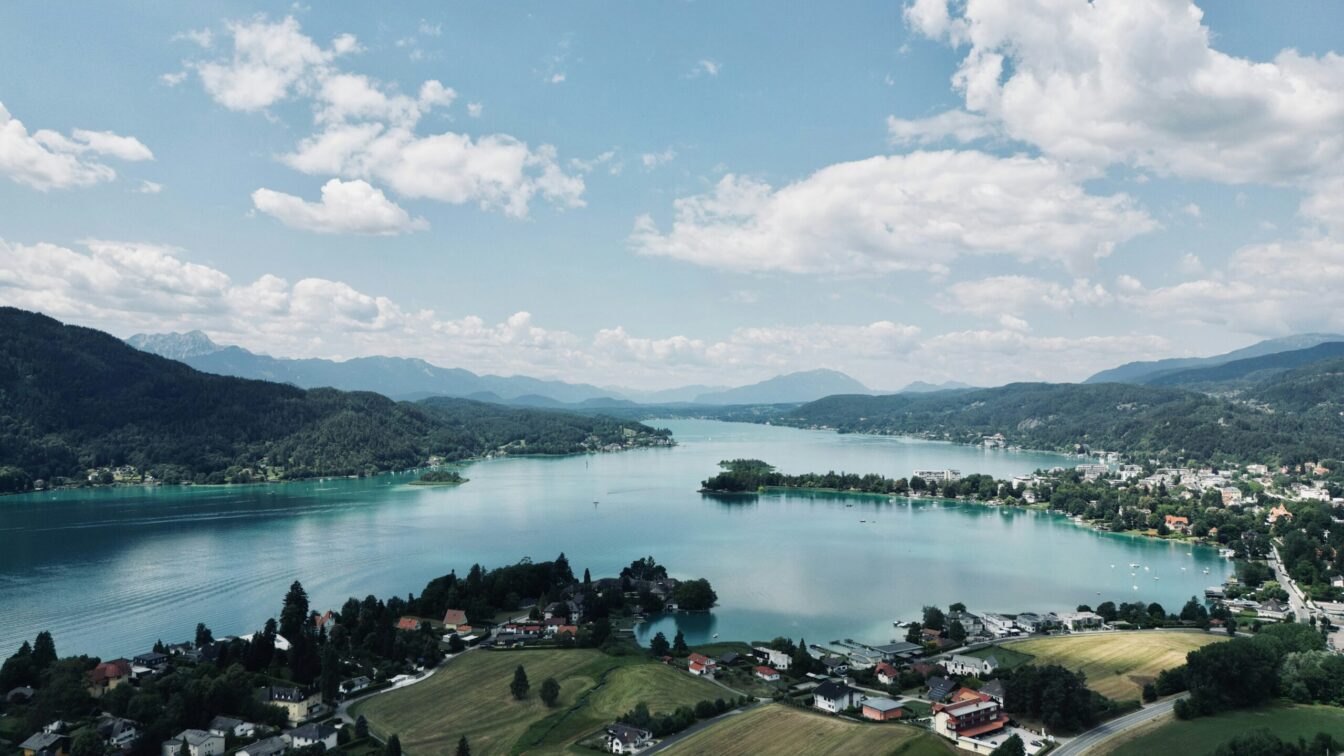 Blick auf einen kleinen Ort am See mit hügeliger Landschaft im Hintergrund