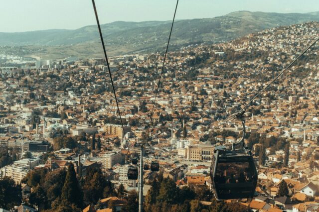 Blick aus einer Seilbahn auf Sarajevo mit zahlreichen Häusern, Hotels und Unterkünften, die sich über die Stadt und die umliegenden Hügel erstrecken.