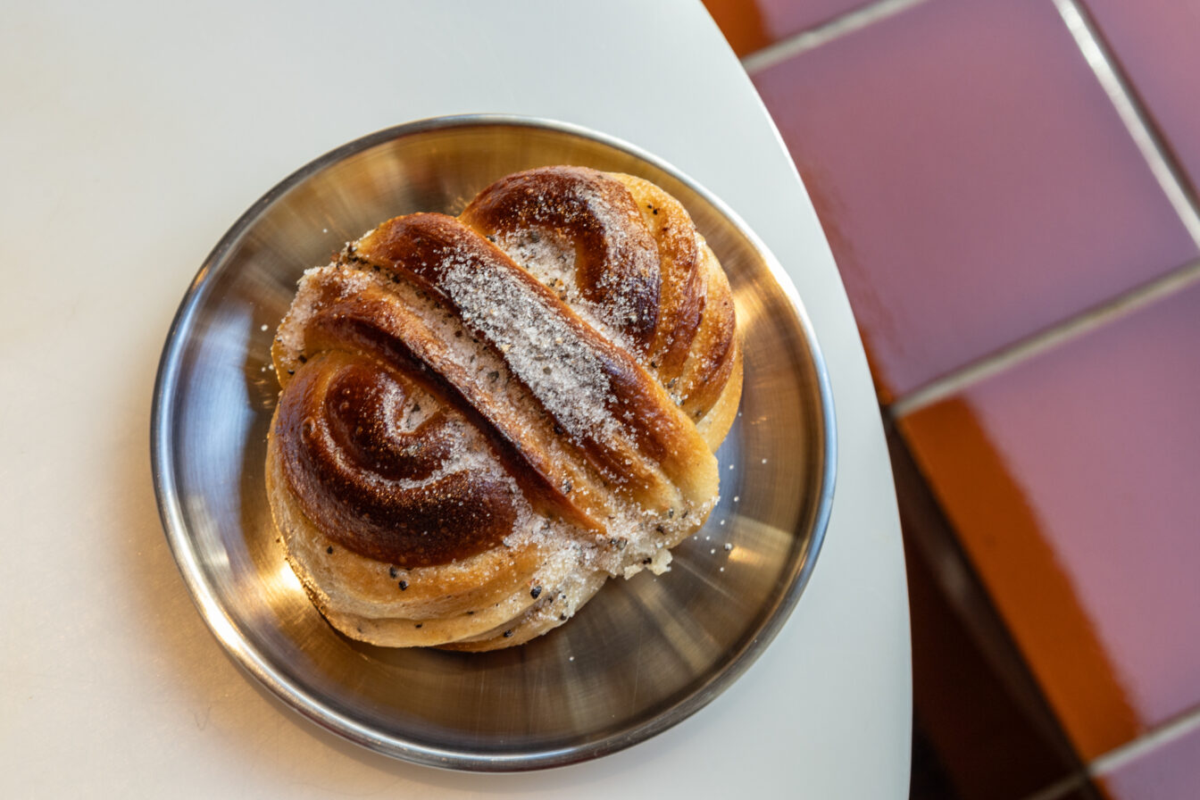Frisch gebackene, goldbraune Kardamomschnecke mit Zuckerguss auf einem Metallteller im Café Acid in Berlin Prenzlauer Berg, bekannt für Specialty Coffee und handgemachtes Gebäck.