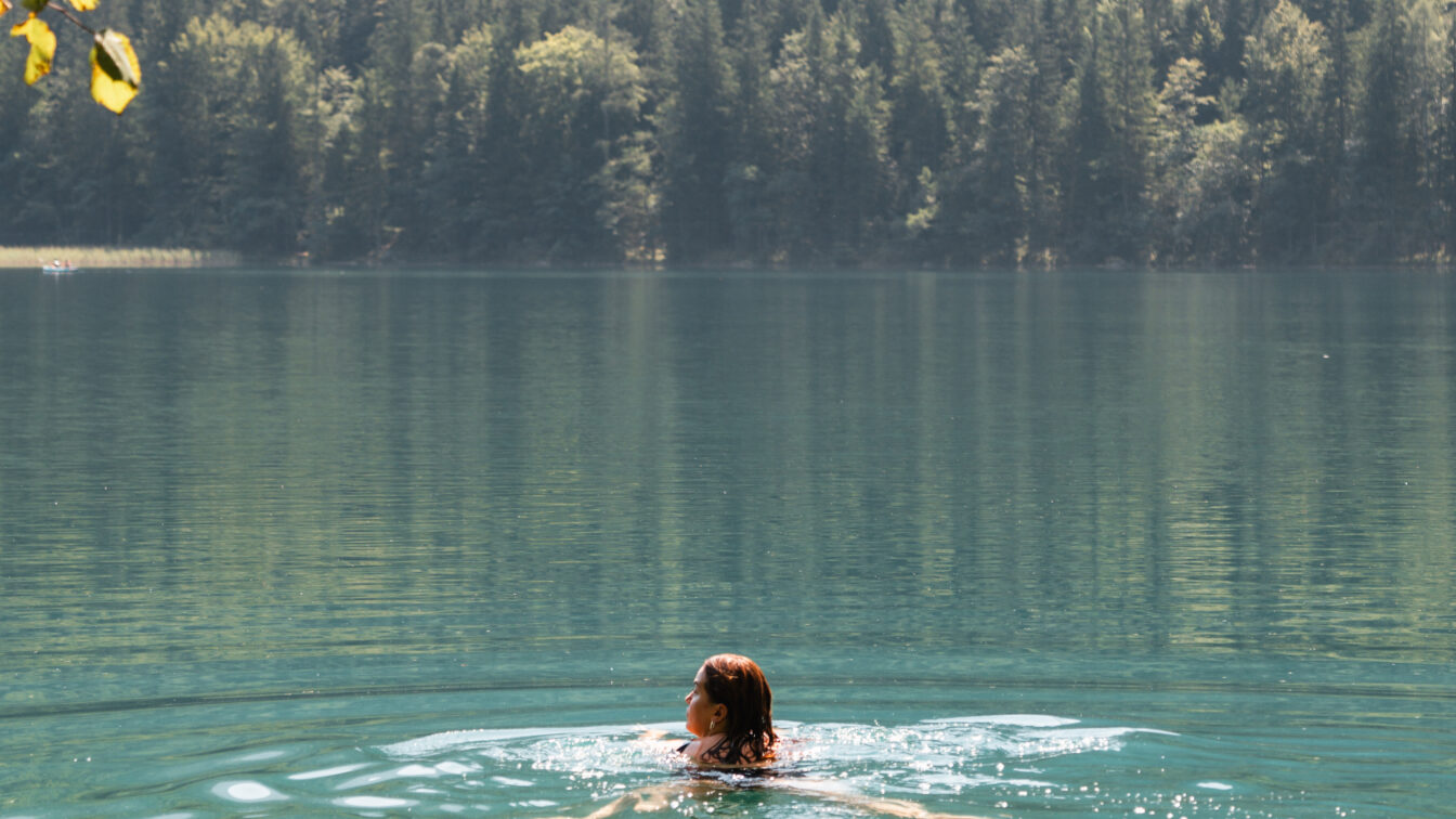 Baden im türkisblauen See mit Wald im Hintergrund