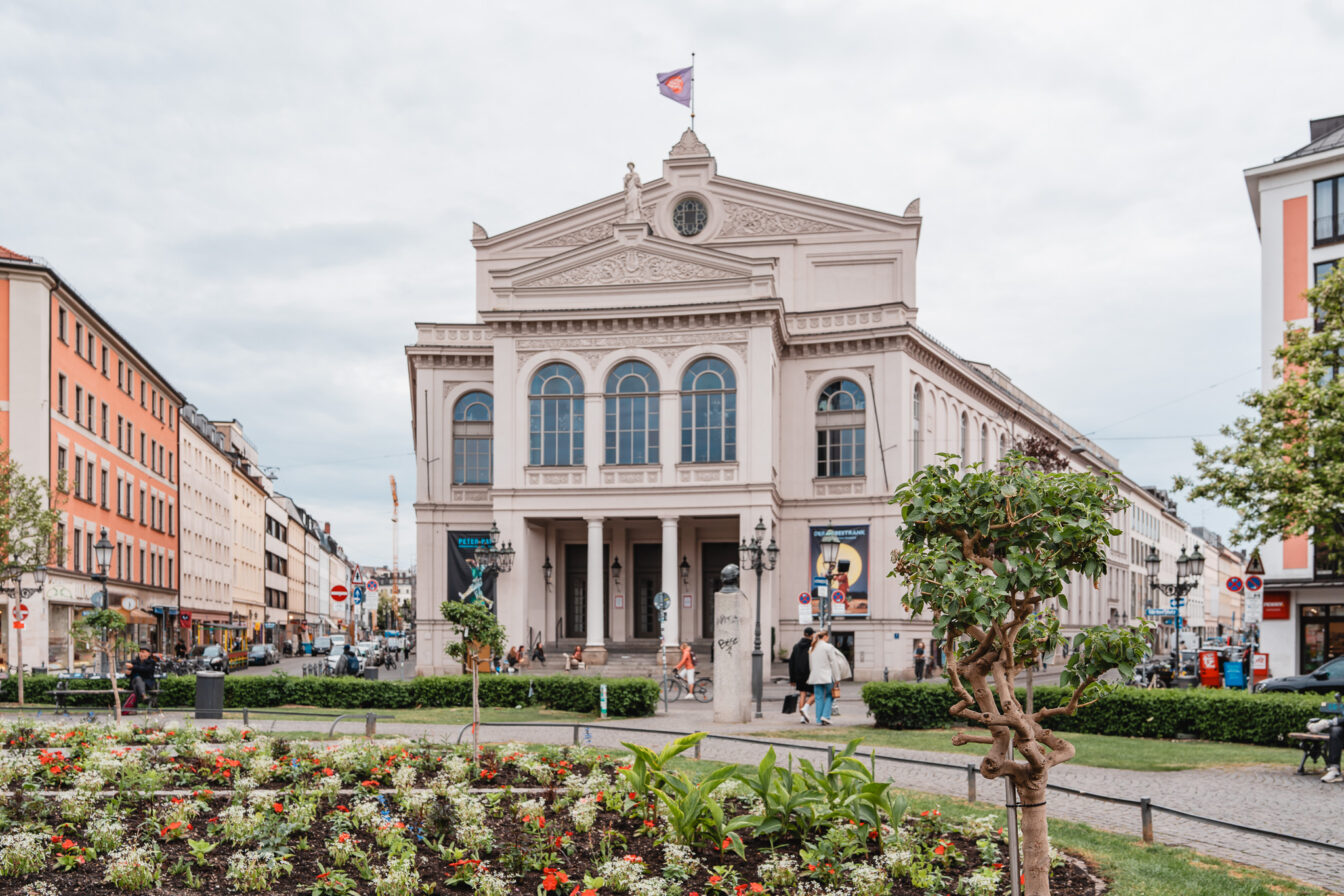 Blumenbeete auf einem runden Platz vor einem imposanten Theater im Glockenbachviertel München.