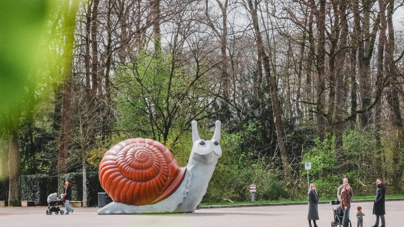 Eine übergroße Schneckenfigur am Eingang eines Parks umgeben von Familien