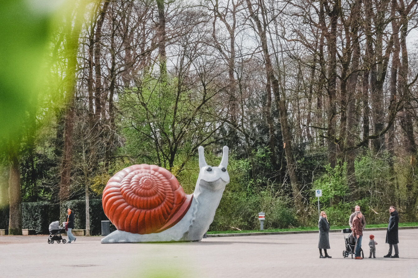 Eine übergroße Schneckenfigur am Eingang eines Parks umgeben von Familien