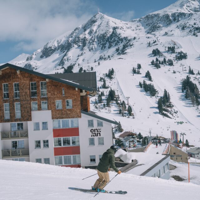 Blick auf das Hotel Enzian in Obertauern mit einem Skifahrer auf der Piste davor.