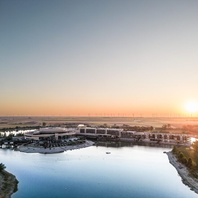 Außenaufnahme der St. Martins Therme & Lodge m Burgenland vor einem Badesee bei Sonnenuntergang.