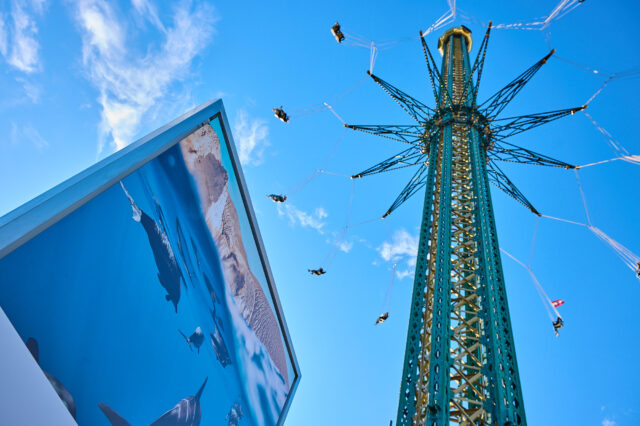 Eine von unten fotografierte Tafel mit einem Foto neben einem hohen kettenkarrussell