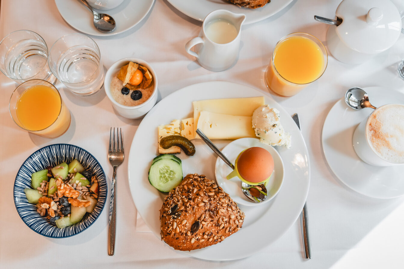 Ein voll gedeckter Frühstückstisch im Hotel in München mit Orangensaft, Ei, Semmel und mehr.