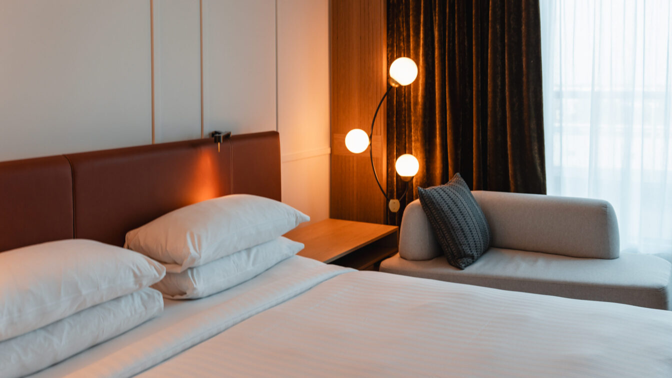 Ein gemachtes Hotelbett mit gemütlichem Licht und Vorhängen zum Balkon.