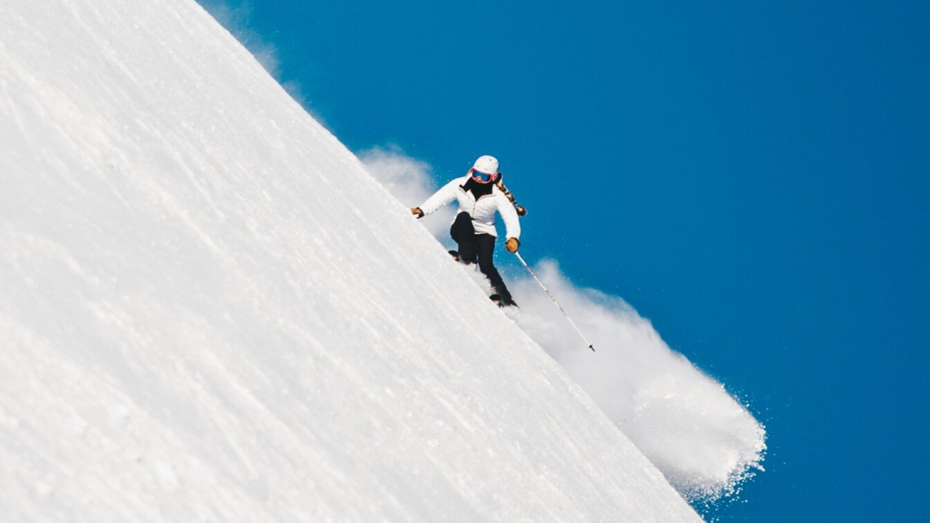 Skifahren in Bayern auf einer steilen Piste bei strahlend blauem Himmel – perfekte Wintersportbedingungen in beliebten Skigebieten wie Garmisch-Partenkirchen, Spitzingsee oder Sudelfeld, die bequem mit den Öffentlichen Verkehrsmitteln erreichbar sind.
