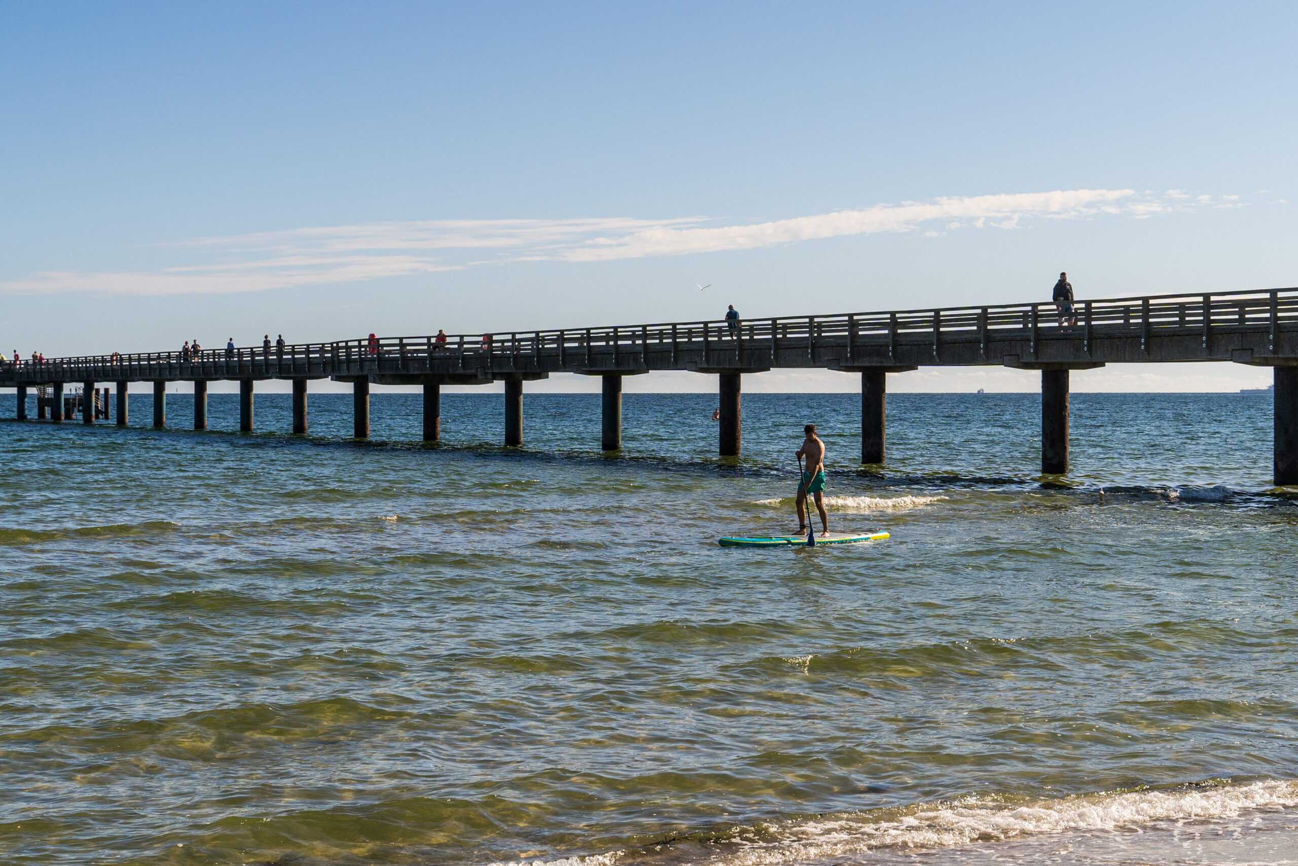 Ein Mann paddelt am Meer unter einer Brücke durch