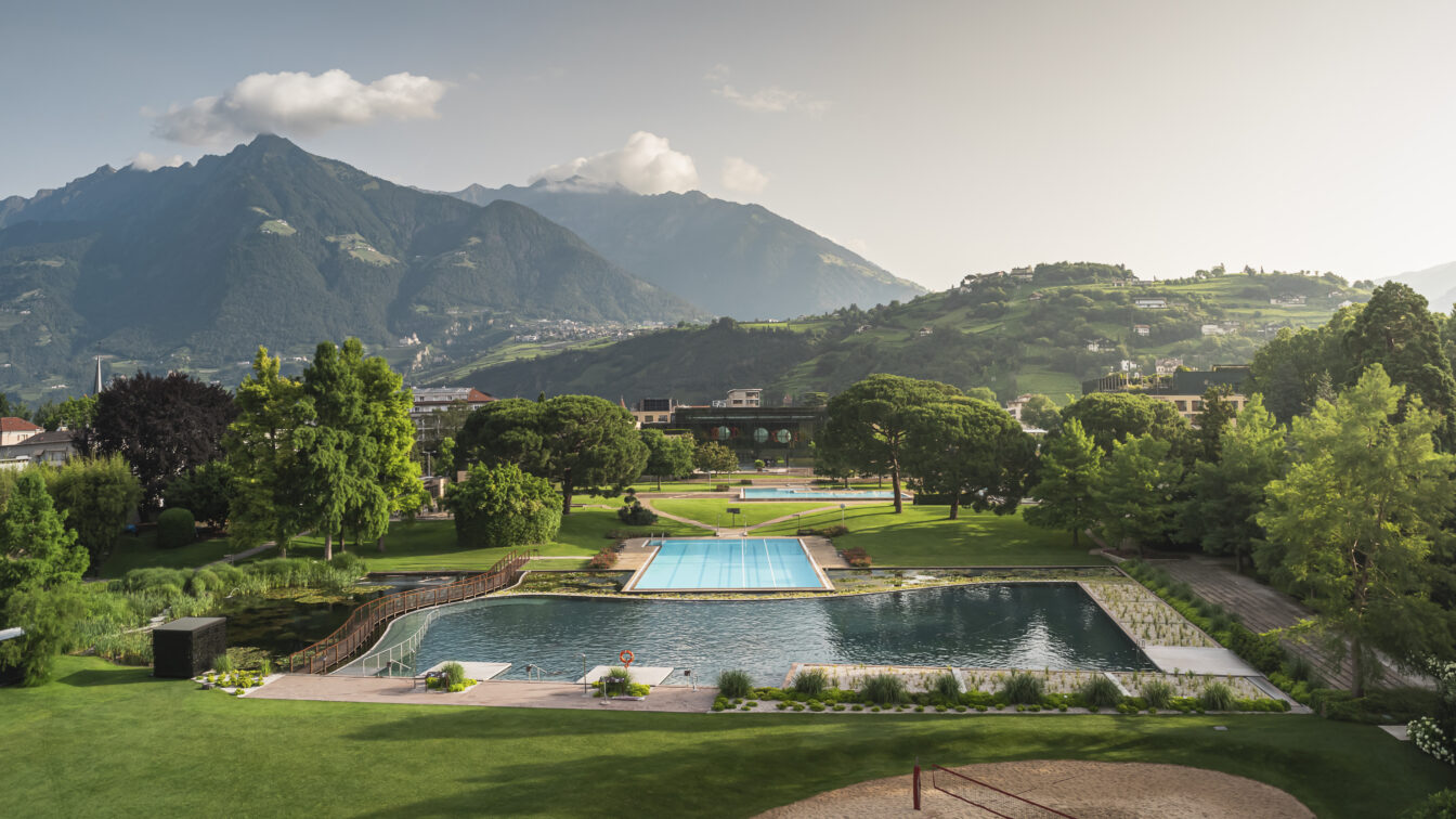 Therme Meran in Südtirol mit Außenpools und weitläufiger Parkanlage, umgeben von grünen Hügeln und imposanten Alpen im Hintergrund – ideal für Wellness, Entspannung und Naturerlebnis.
