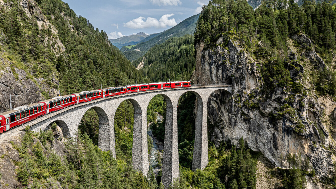 Ein Zug fährt über eine hohe Brücke in den Bergen